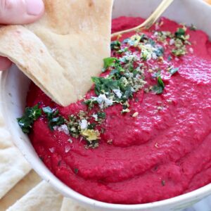 beet hummus in bowl with piece of pita bread dipped into the hummus